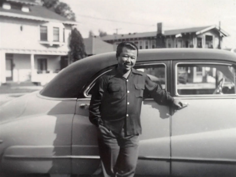 Fujita, smiling and standing in front of a car.